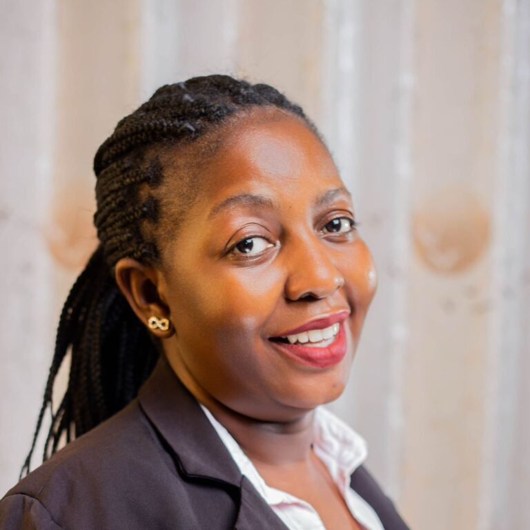 Smiling woman with long braided hair wearing a dark blazer and white blouse against a plain light background